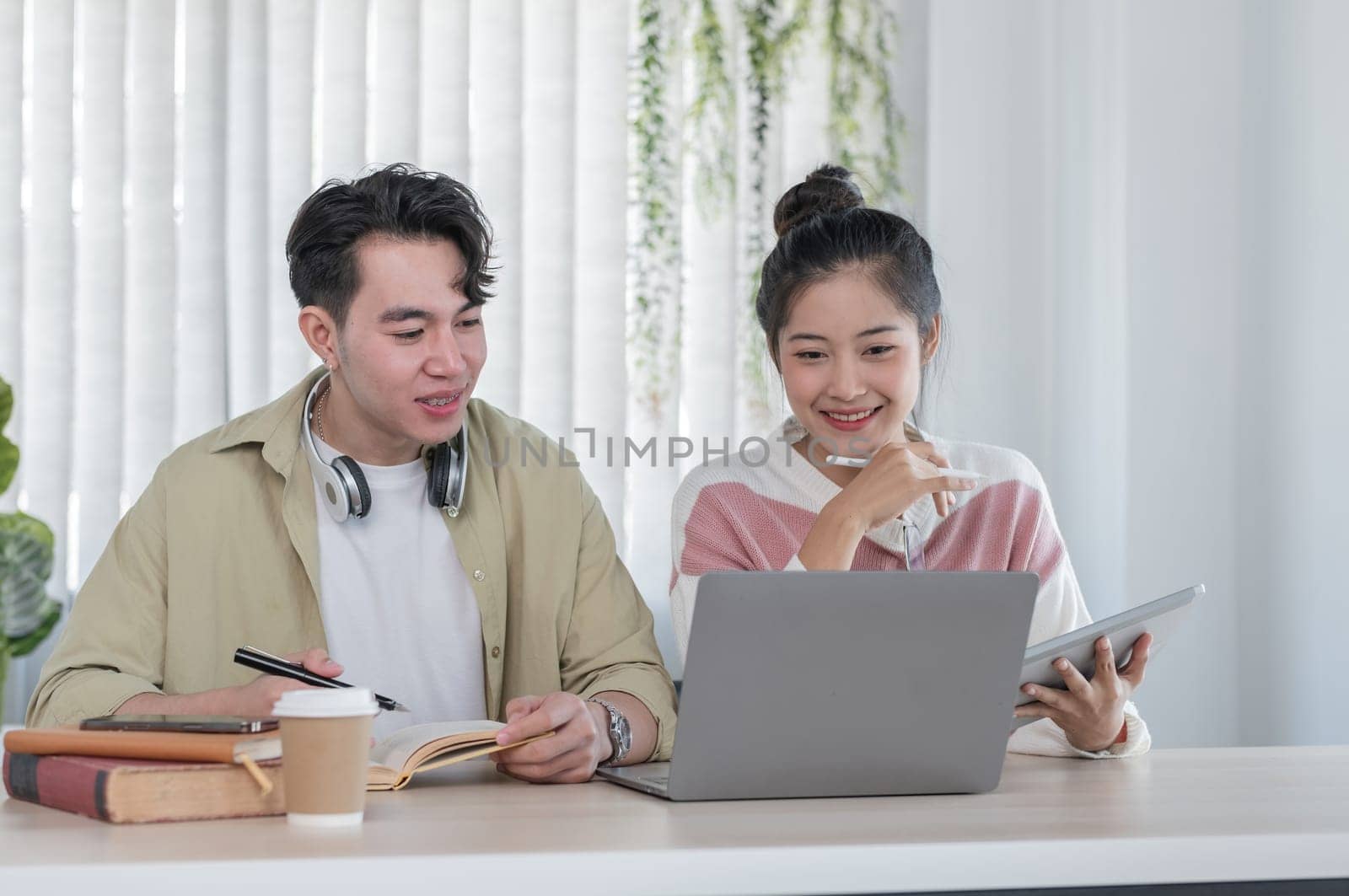 Two students studying together online, using laptops and books, in a bright and modern home environment.