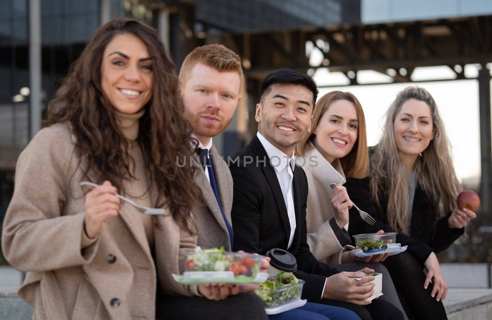 Side view of diverse business people enjoying a lunch break outdoor from office building and looking at camera by papatonic