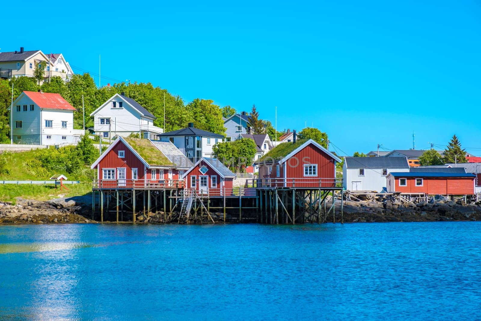 Charming coastal village in Norway with traditional red wooden cabins on stilts offer unique views of serene water and landscape. Reine, Lofoten, Norway