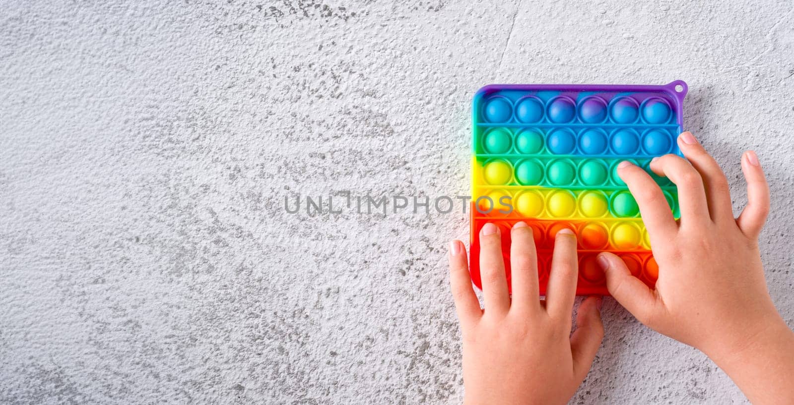 Top view of rainbow antistress sensory toy fidget push pop it on stone background by Sonat