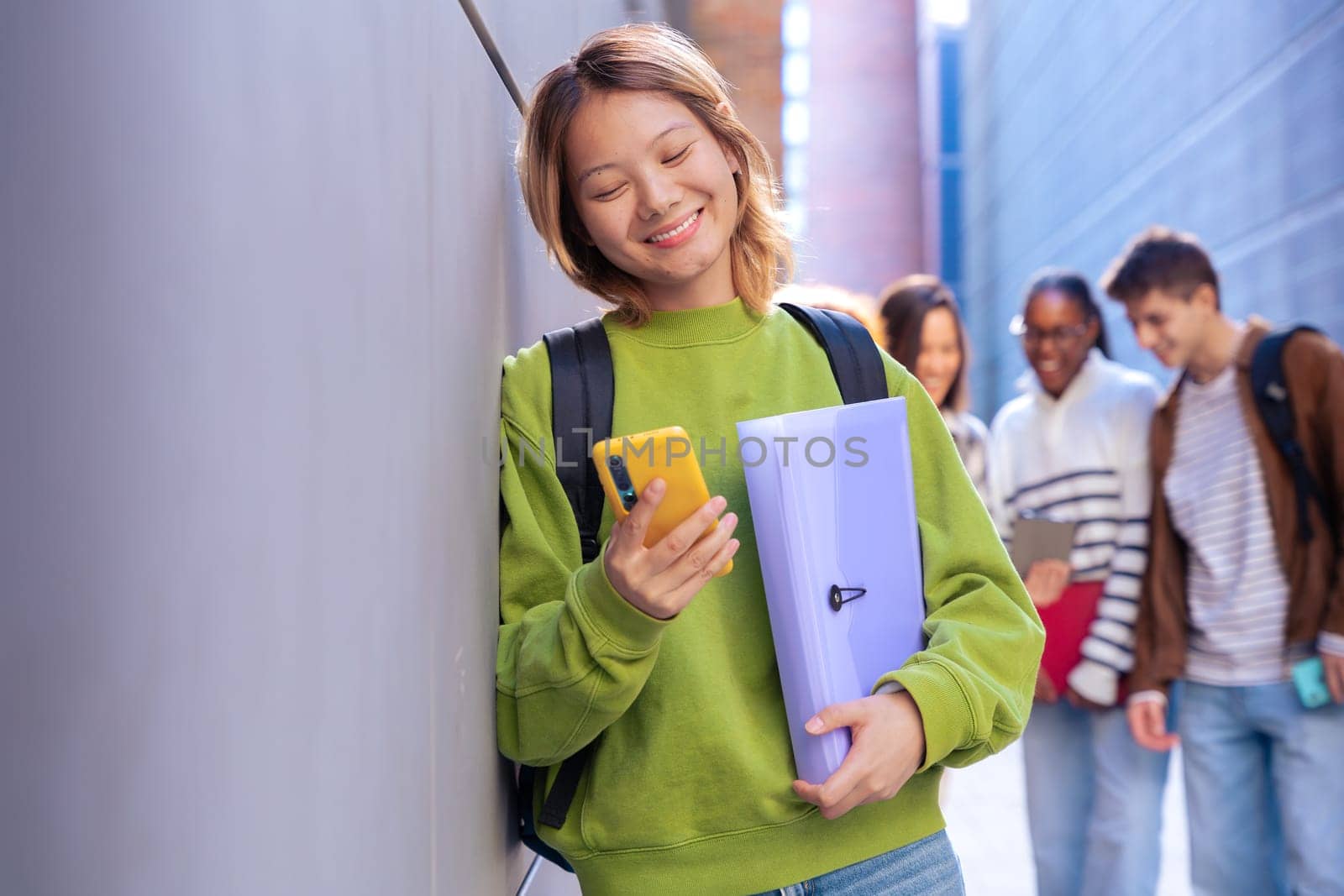 Happy young chinese woman browsing the internet using mobile device outdoors. by mariaphoto3