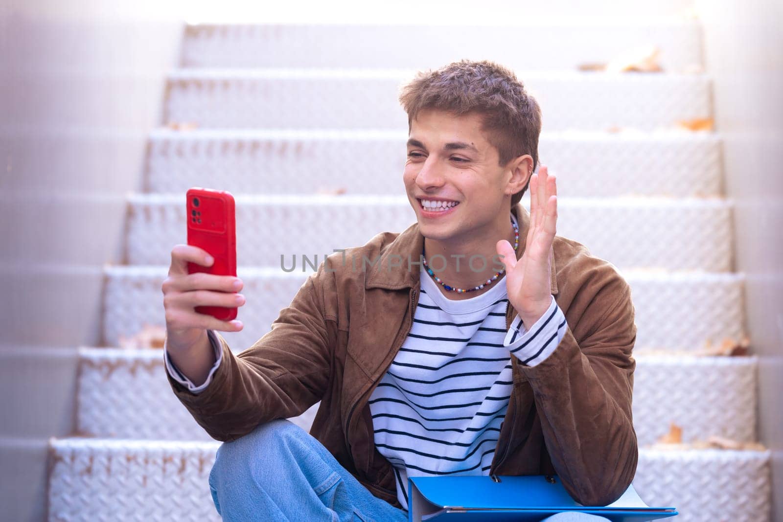 A happy student is on the university campus making a video call with a mobile phone. College life