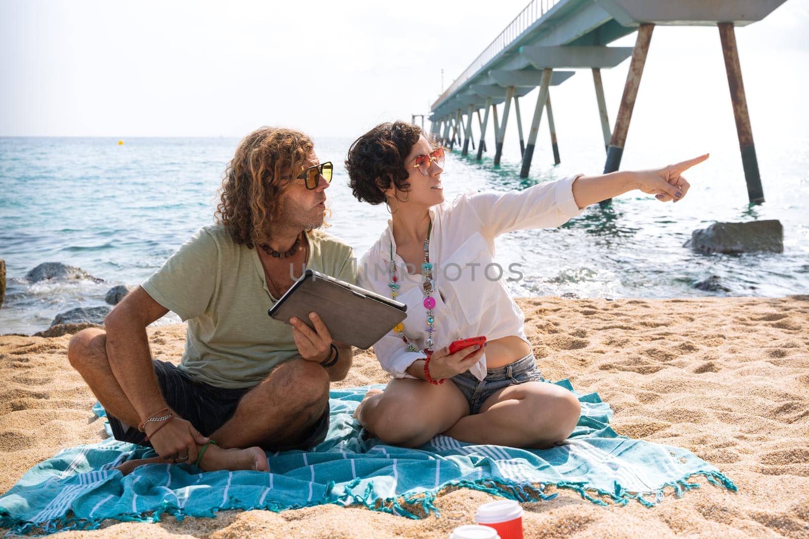 Couple on the beach,pointing to the location of the hotel with the tablet by molesjuny