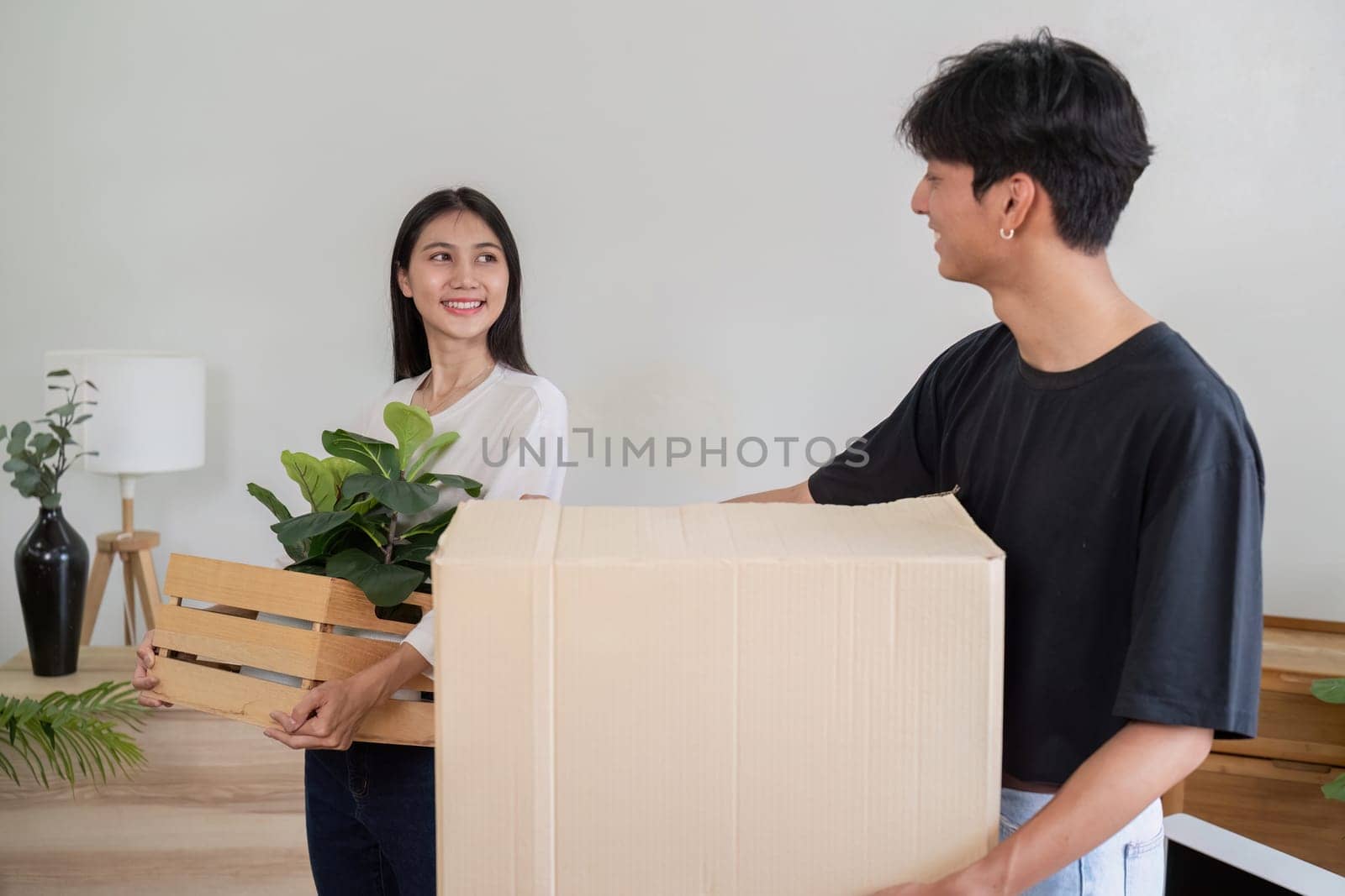 A young couple happily moving into their new house, carrying boxes and plants, symbolizing a fresh start in a modern home.