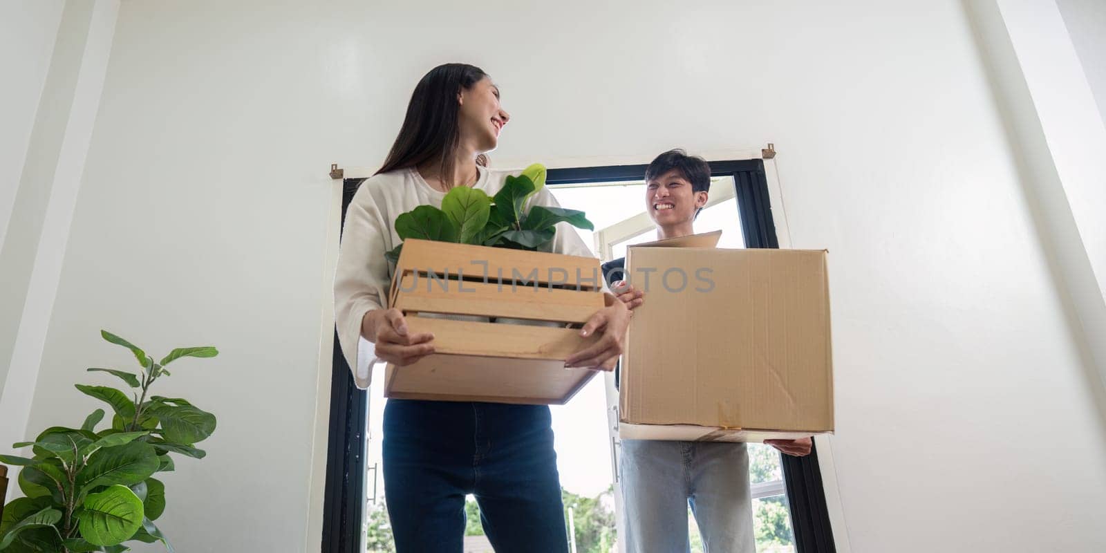 A young couple happily moving into their new house, carrying boxes and plants, symbolizing a fresh start in their modern home.