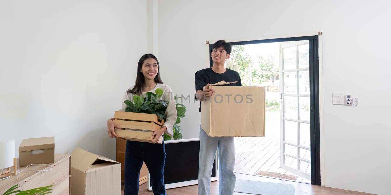 A joyful couple carrying boxes and plants into their new home, symbolizing a fresh start and new beginnings.