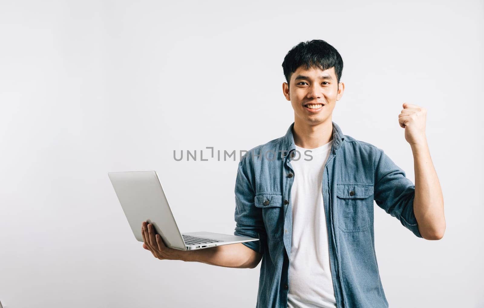 Portrait smiling Asian young man hold a laptop computer studio shot isolated white background, happiness and excited man holding laptop and raising his arm up by Sorapop