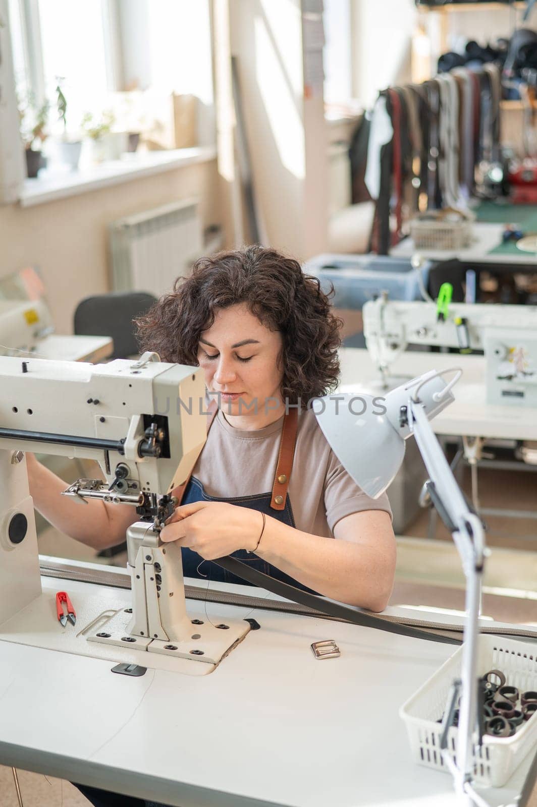 A woman tanner sews a leather belt on a sewing machine. Vertical photo. by mrwed54