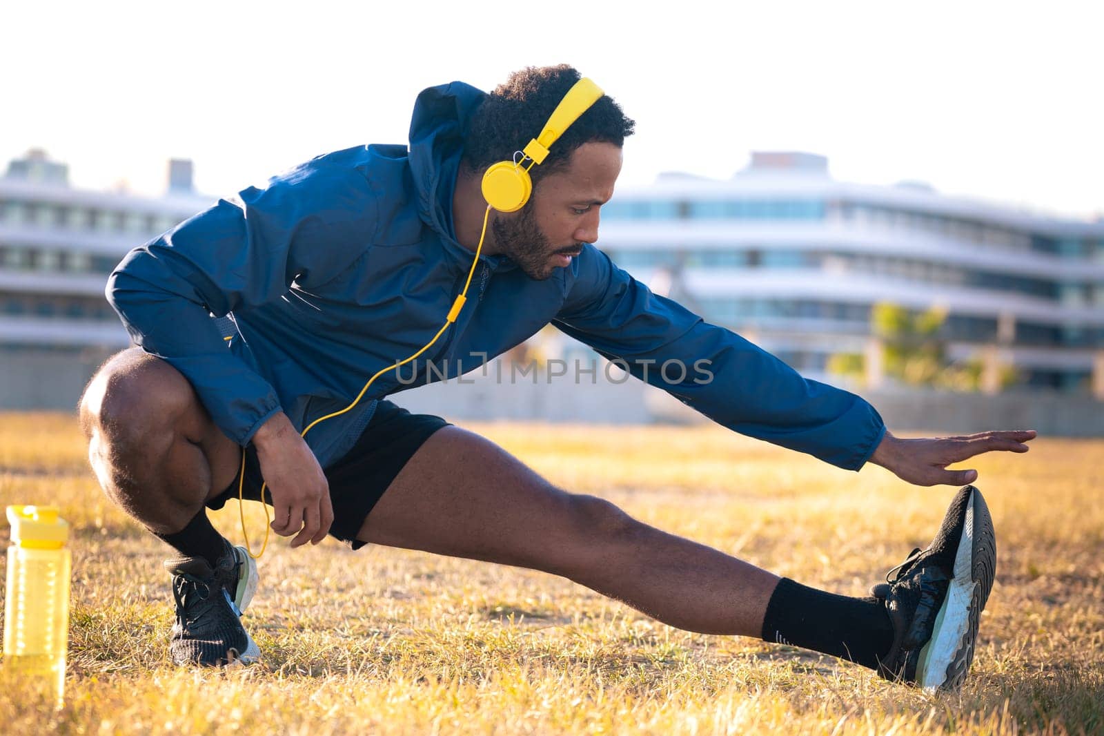 Young latin sportsman with sports headphones doing stretches with water bottle on the floor.