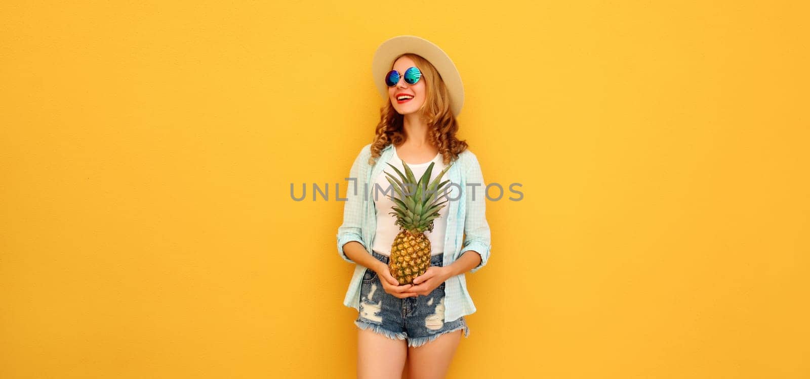 Summer vacation, happy joyful young woman with pineapple fruit in tourist hat, cheerful girl posing on yellow studio background