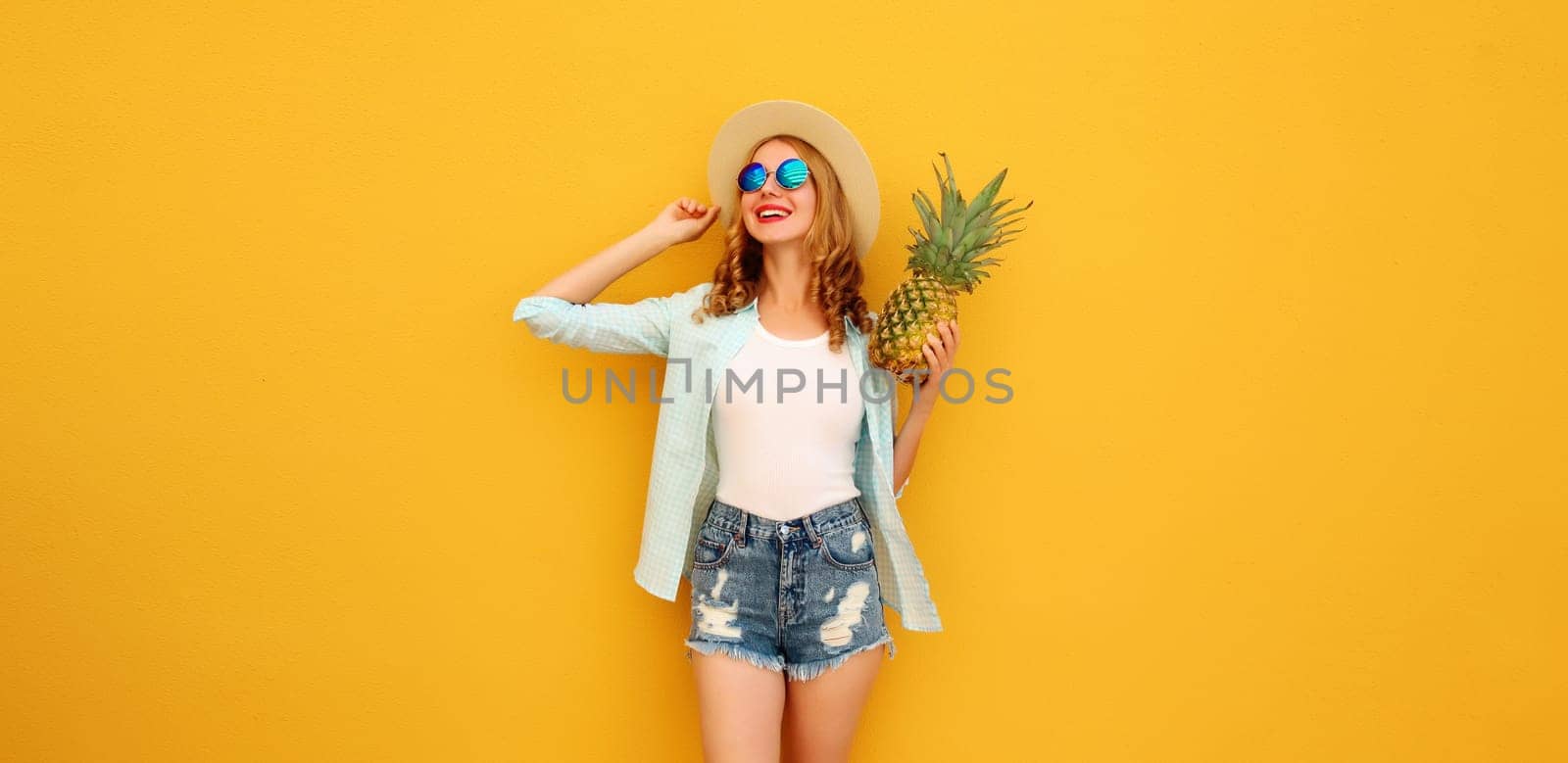 Summer vacation, happy joyful young woman with pineapple fruit in tourist hat, cheerful girl posing on yellow studio background