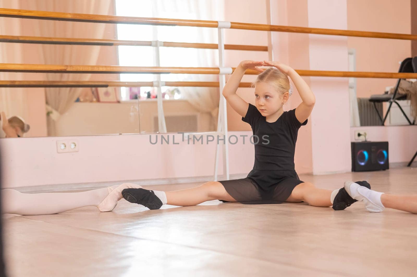 Little girls sit in a circle and do stretching at a ballet school