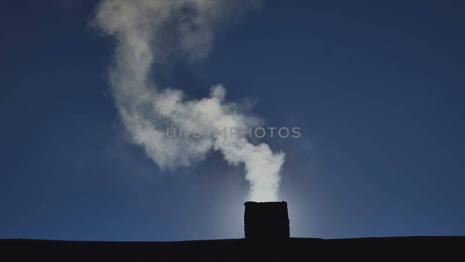 Silhouette of smoke against the sun from the chimney of a village house