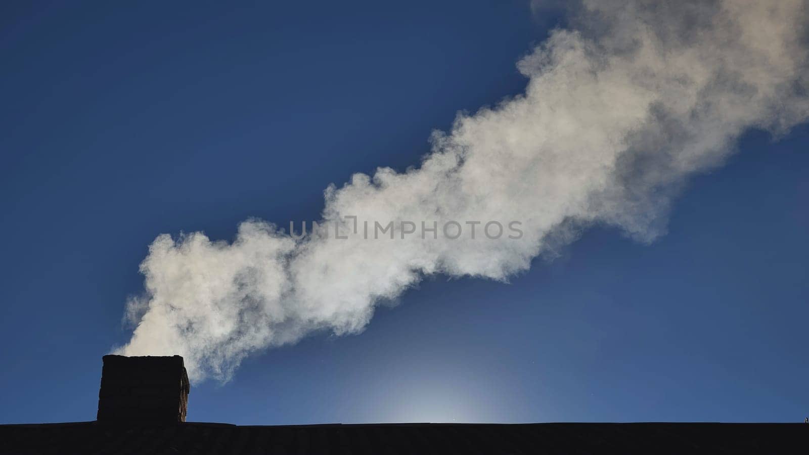 Silhouette of smoke against the sun from the chimney of a village house