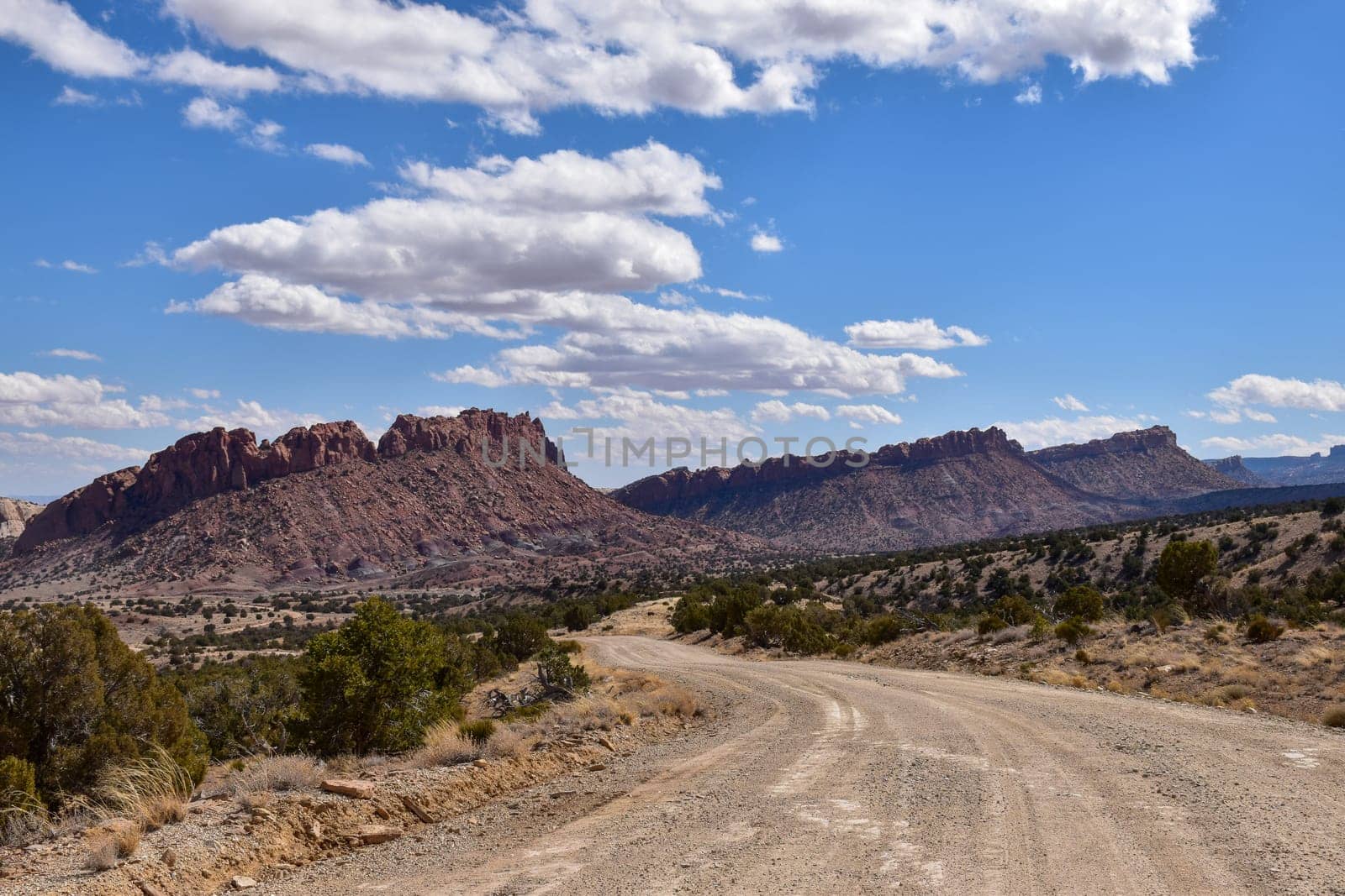Scenic view of Capitol Reef National Park in Utah featuring the majestic Waterpocket Fold under a blue sky with scattered clouds. The winding dirt road is known as the Burr Trail - USA