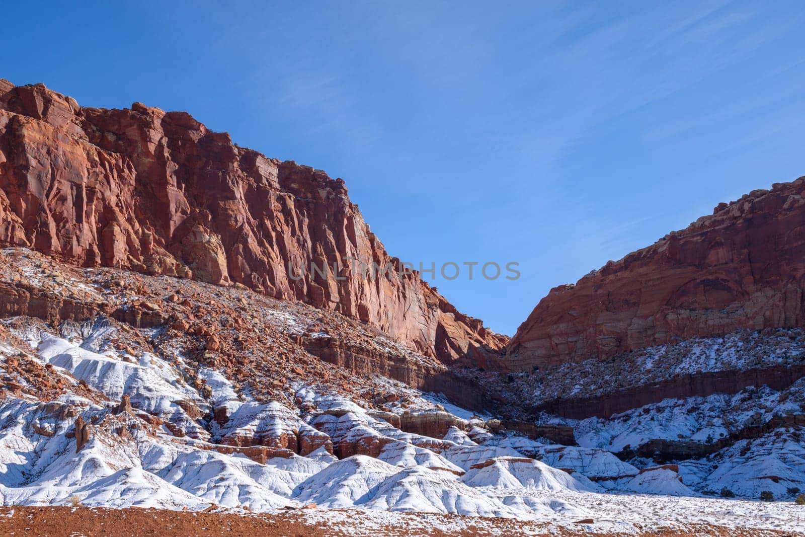 Beautiful winter scene of Capitol Reef in Utah with snow-covered rock formations. The red and white contrast against a clear blue sky showcases nature's beauty. Perfect for nature and travel - Utah