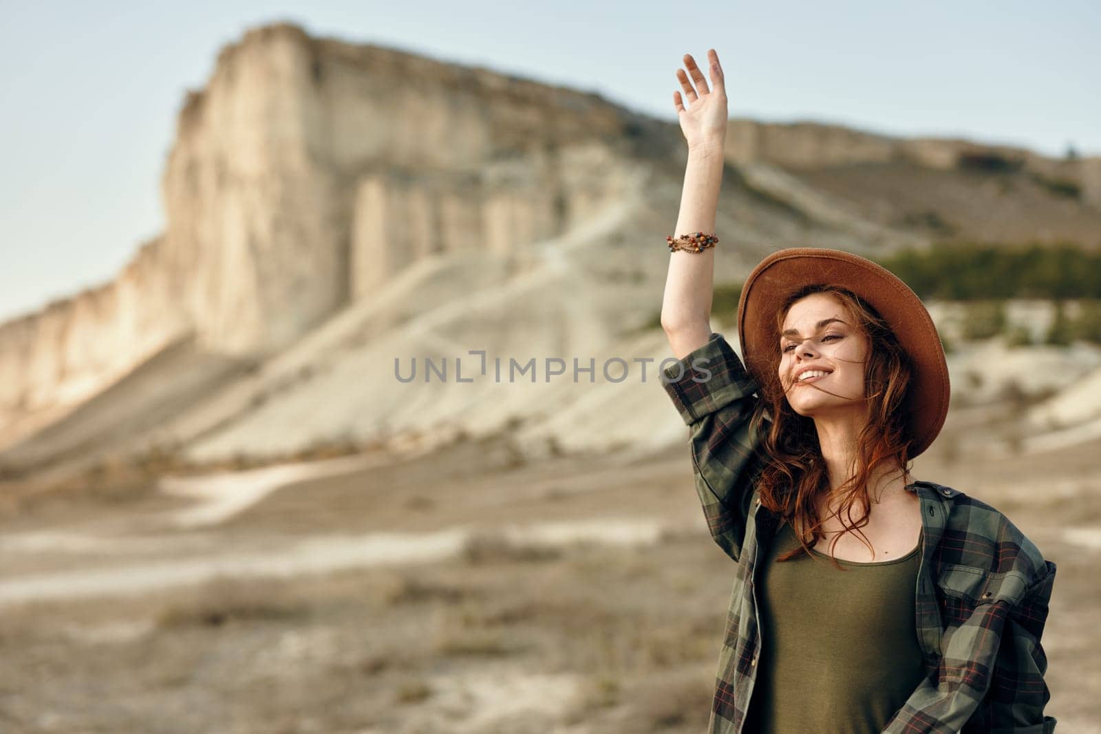 Exhilarated woman in hat celebrating in front of majestic mountain landscape