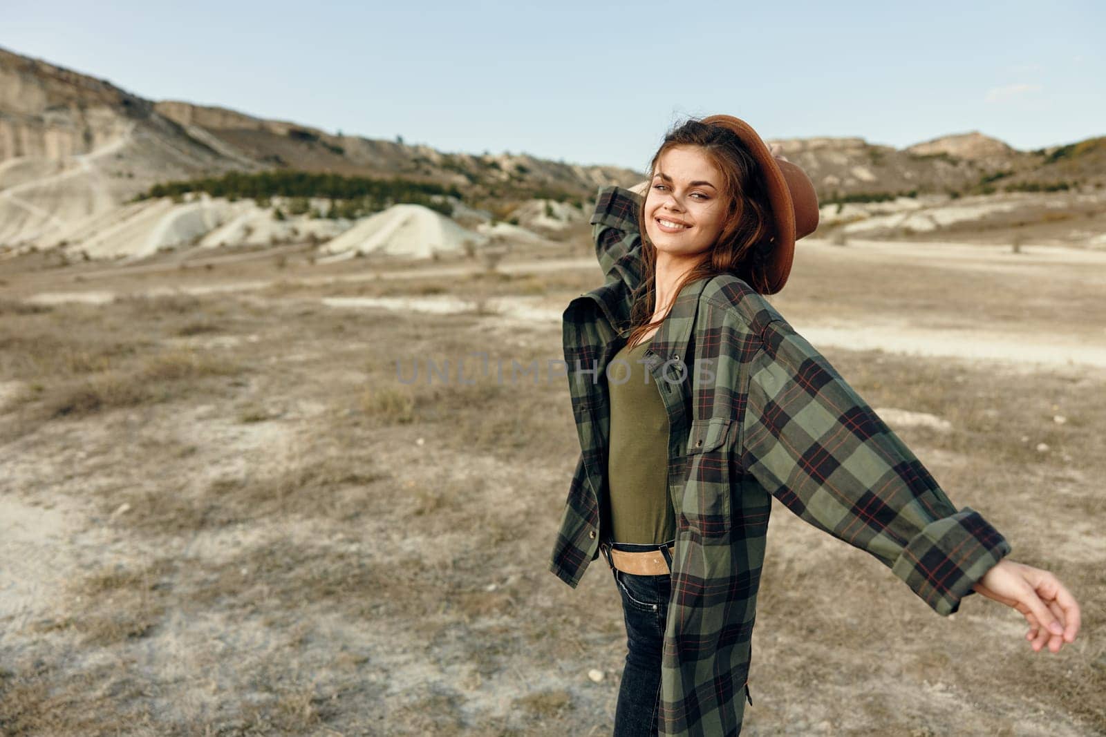 Woman in plaid shirt standing with arms outstretched in the vast field under the open sky