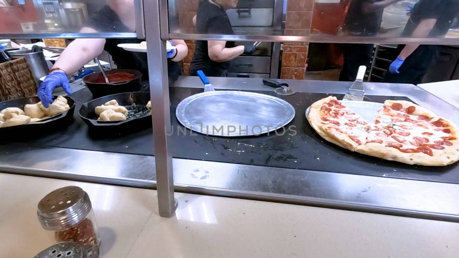 Colorado Springs, Colorado, USA-June 12, 2024-Slow motion-Close-up of a freshly baked pizza slice on a paper plate, placed on a black tray in a pizzeria. The background shows more pizzas being prepared, creating a warm and inviting atmosphere.