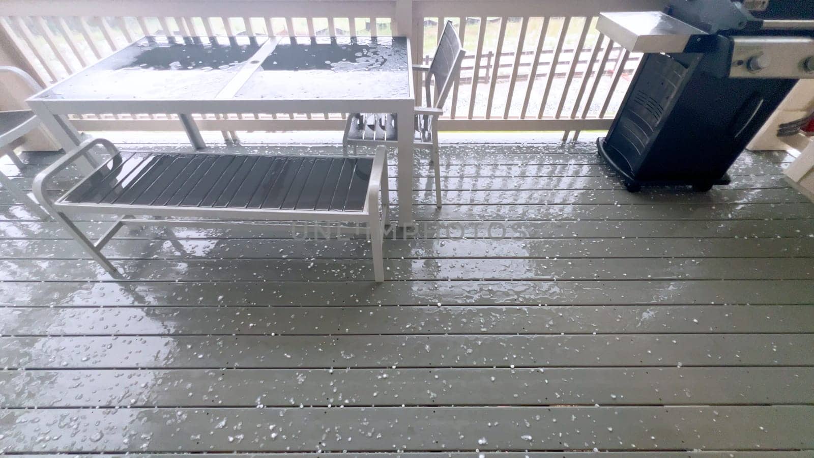 Castle Rock, Colorado, USA-June 12, 2024-Slow motion-Image capturing a hail storm on a wooden deck, highlighting the impact of hail on patio furniture and the deck surface. Hailstones are visible scattered across the wet deck, with patio furniture in the background.