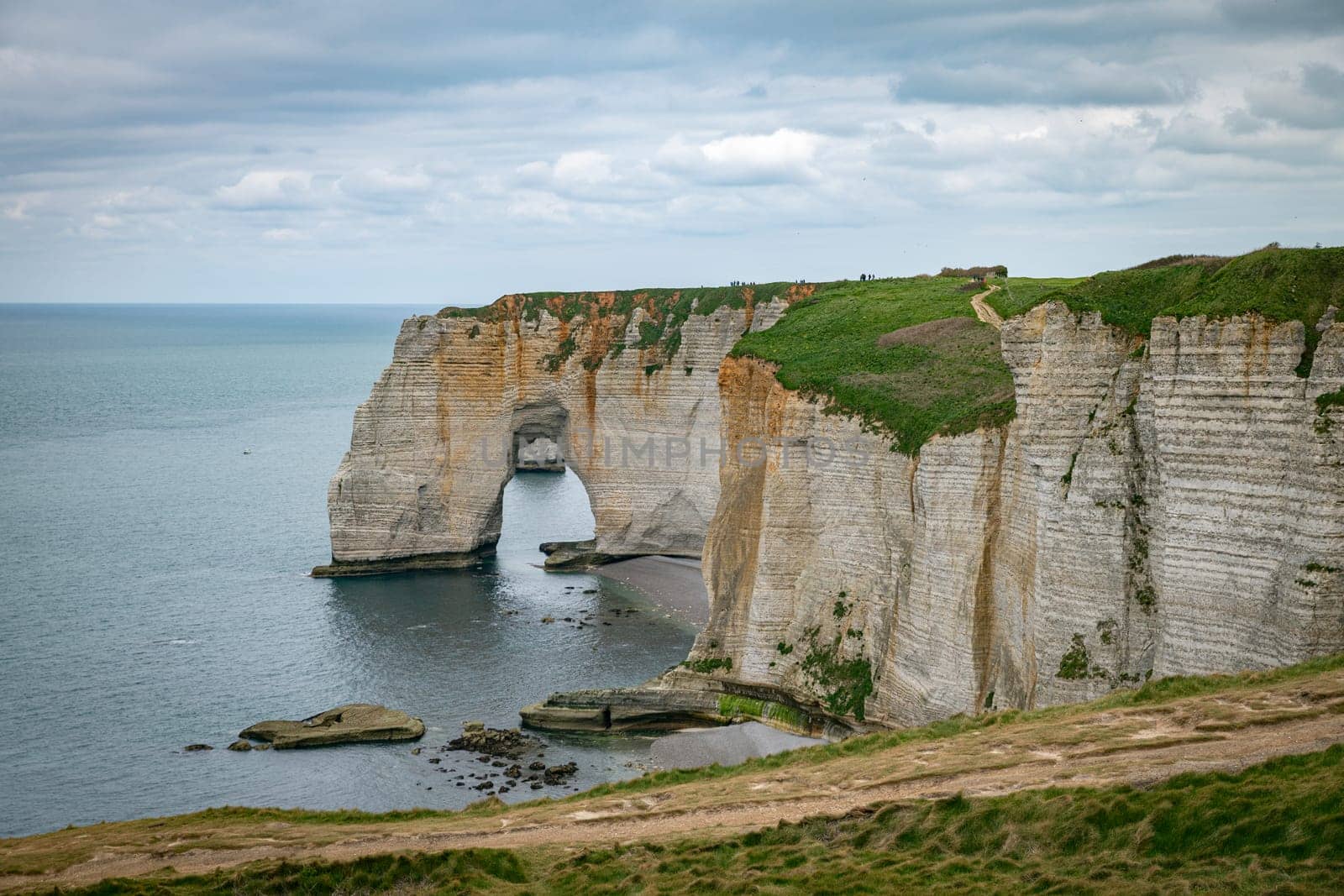 Landscape photo of tall, steep limestone cliffs by the ocean with one with a hole in it creating an arch