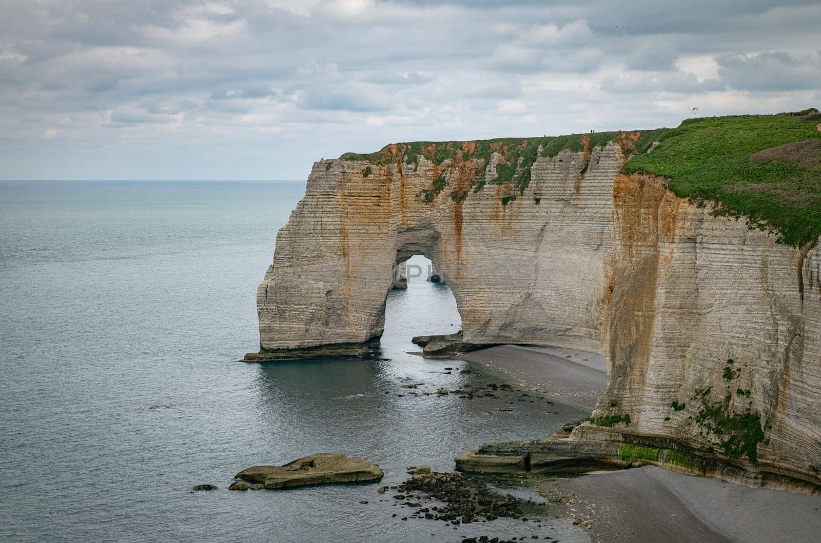 Landscape photo of tall, steep limestone cliffs by the ocean with one with a hole in it creating an arch