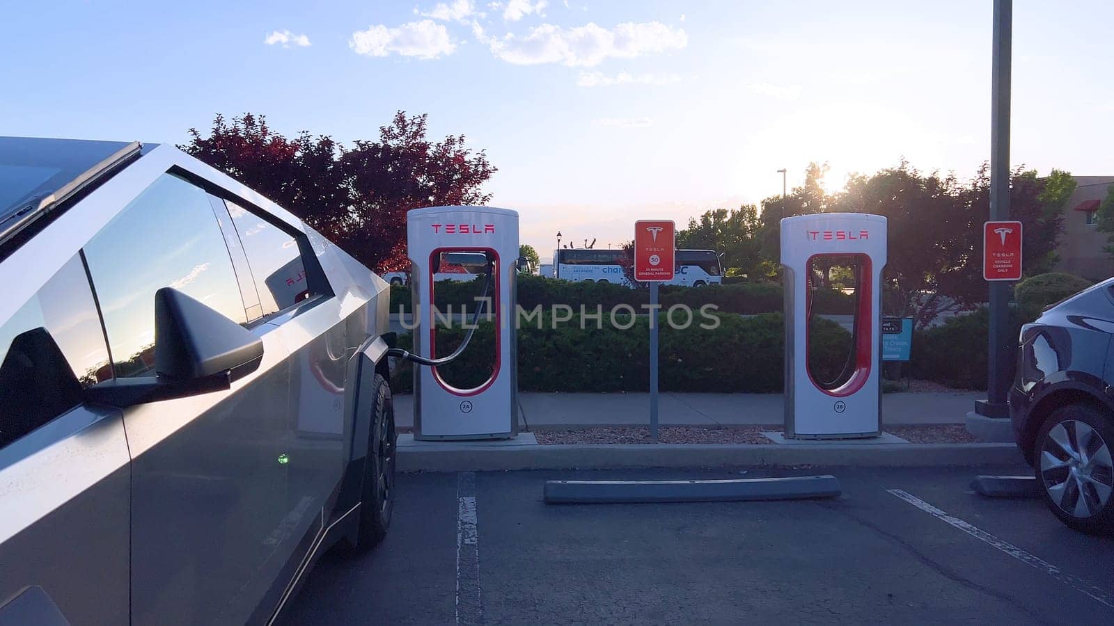 Santa Fe, New Mexico, USA-June 10, 2024-Slow motion-A Tesla Cybertruck is connected to a Tesla Supercharger at an outdoor charging station. The sleek, angular design of the Cybertruck is highlighted by the sunlight, emphasizing its modern and futuristic appearance.