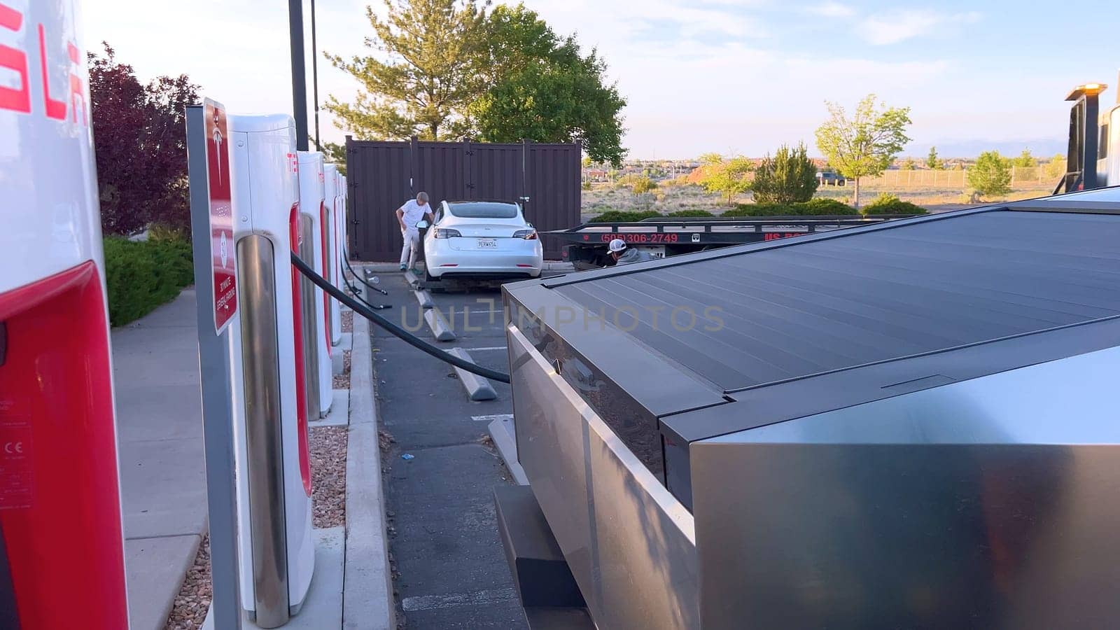 Santa Fe, New Mexico, USA-June 10, 2024-Slow motion-A Tesla Cybertruck is connected to a Tesla Supercharger at an outdoor charging station. The sleek, angular design of the Cybertruck is highlighted by the sunlight, emphasizing its modern and futuristic appearance.
