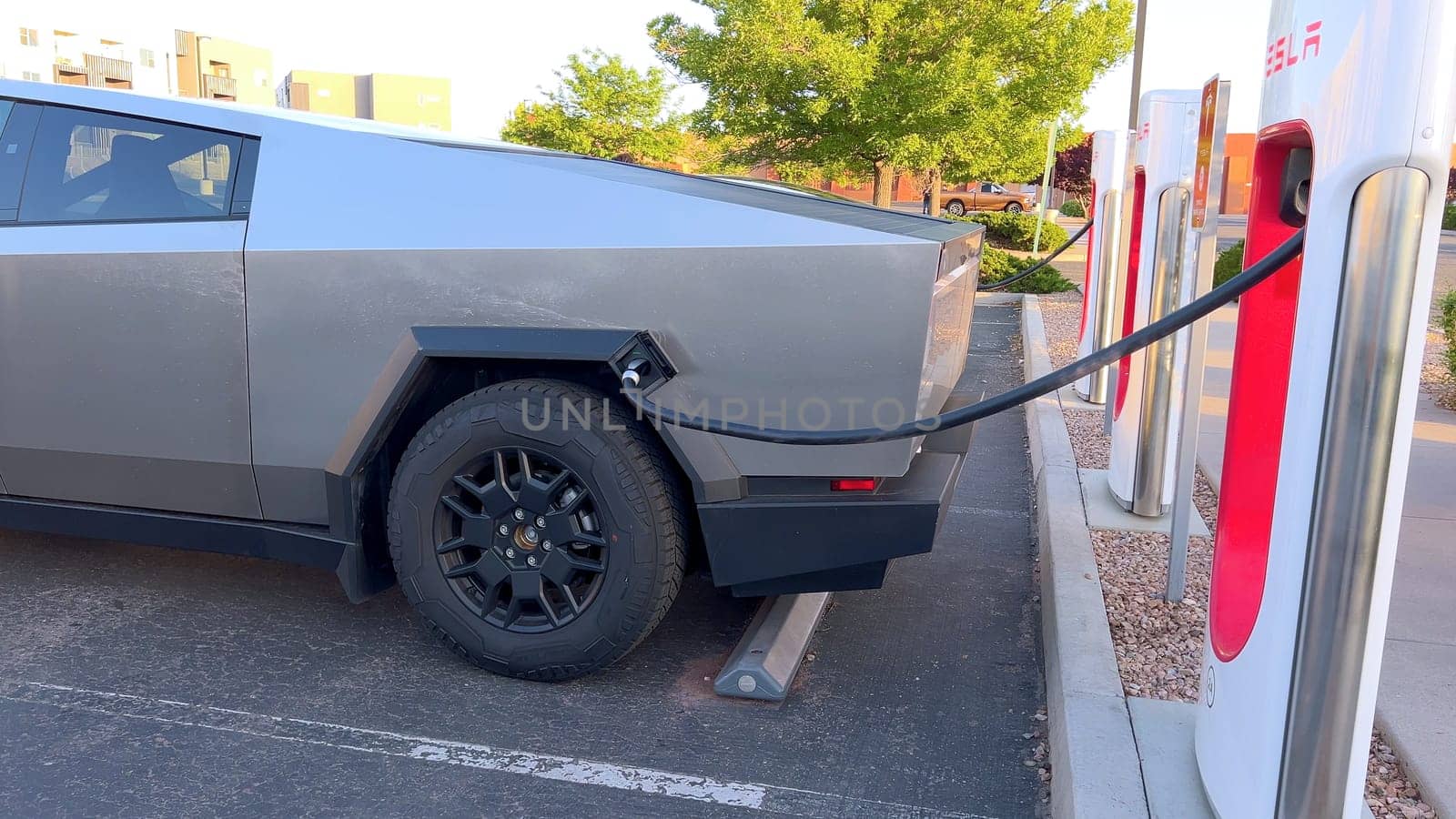 Santa Fe, New Mexico, USA-June 10, 2024-Slow motion-A Tesla Cybertruck is connected to a Tesla Supercharger at an outdoor charging station. The sleek, angular design of the Cybertruck is highlighted by the sunlight, emphasizing its modern and futuristic appearance.