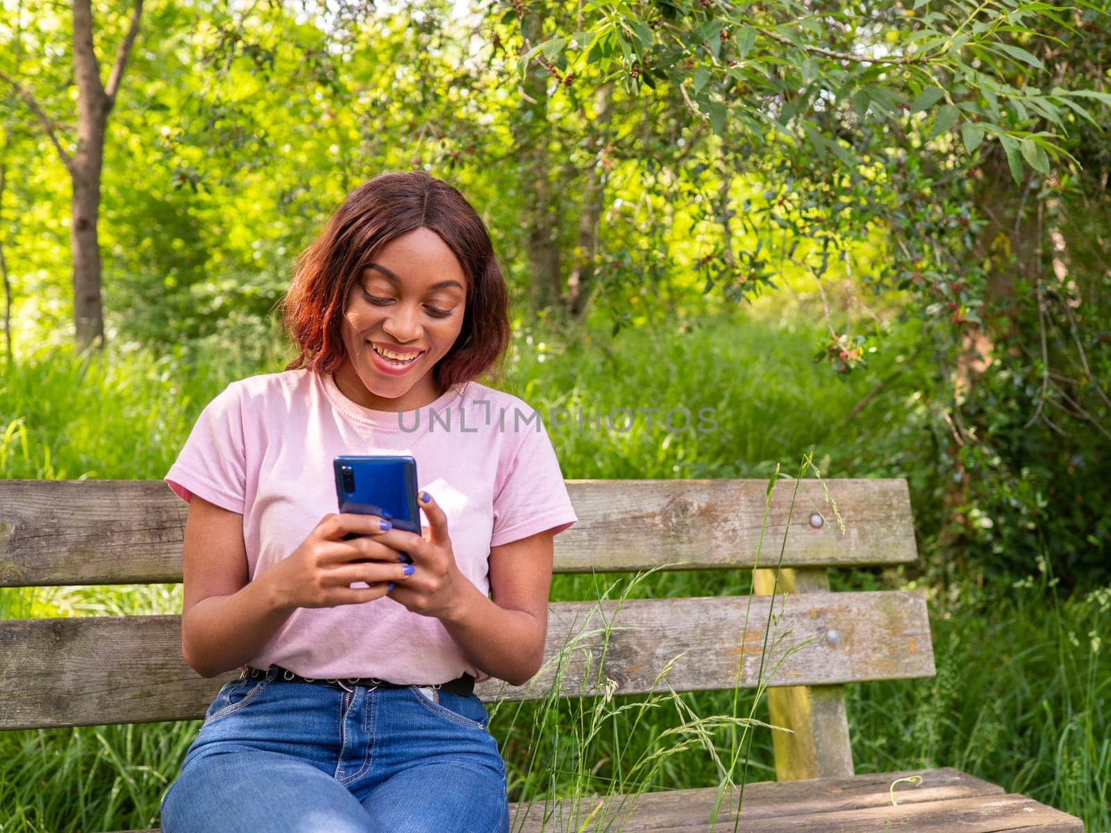 Young black woman with her phone chatting with her friends in a park on an October afternoon. by Ceballos