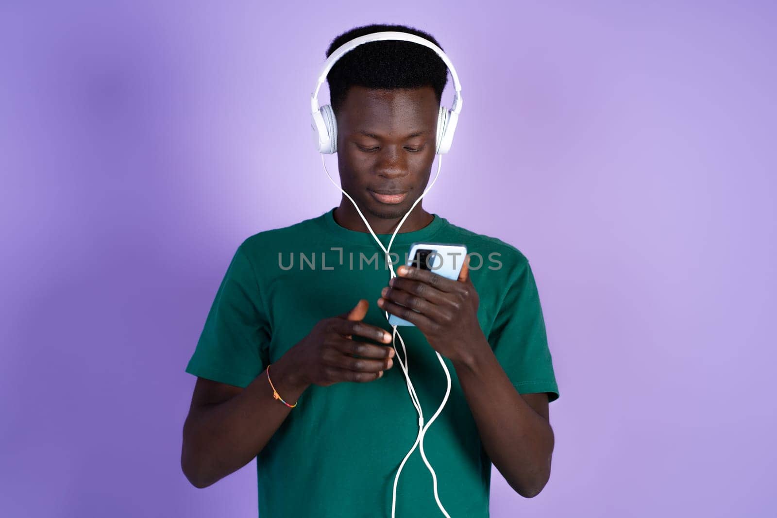 A man wearing headphones is focused on his cell phone screen.