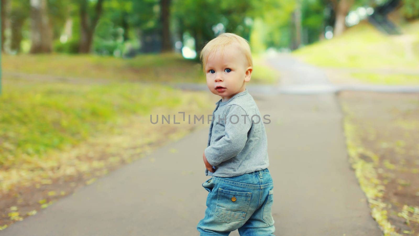 Portrait of caucasian baby little boy walking in summer park and looking at camera