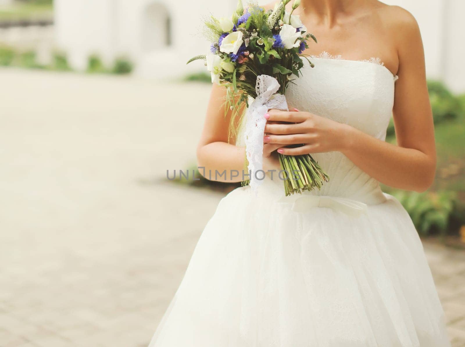 Beautiful lovely bride in white wedding dress holding bouquet of flowers outdoors