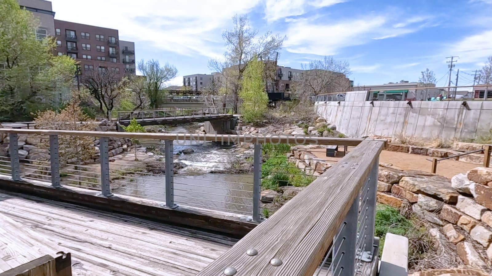 Castle Rock, Colorado, USA-June 12, 2024-Slow motion-A picturesque view of Downtown Castle Rock, Colorado, featuring a serene river flowing through the urban landscape. The scene includes a charming bridge, lush greenery, and modern buildings in the background under a bright blue sky with scattered clouds. The blend of nature and urban development highlights the unique character of this vibrant community.