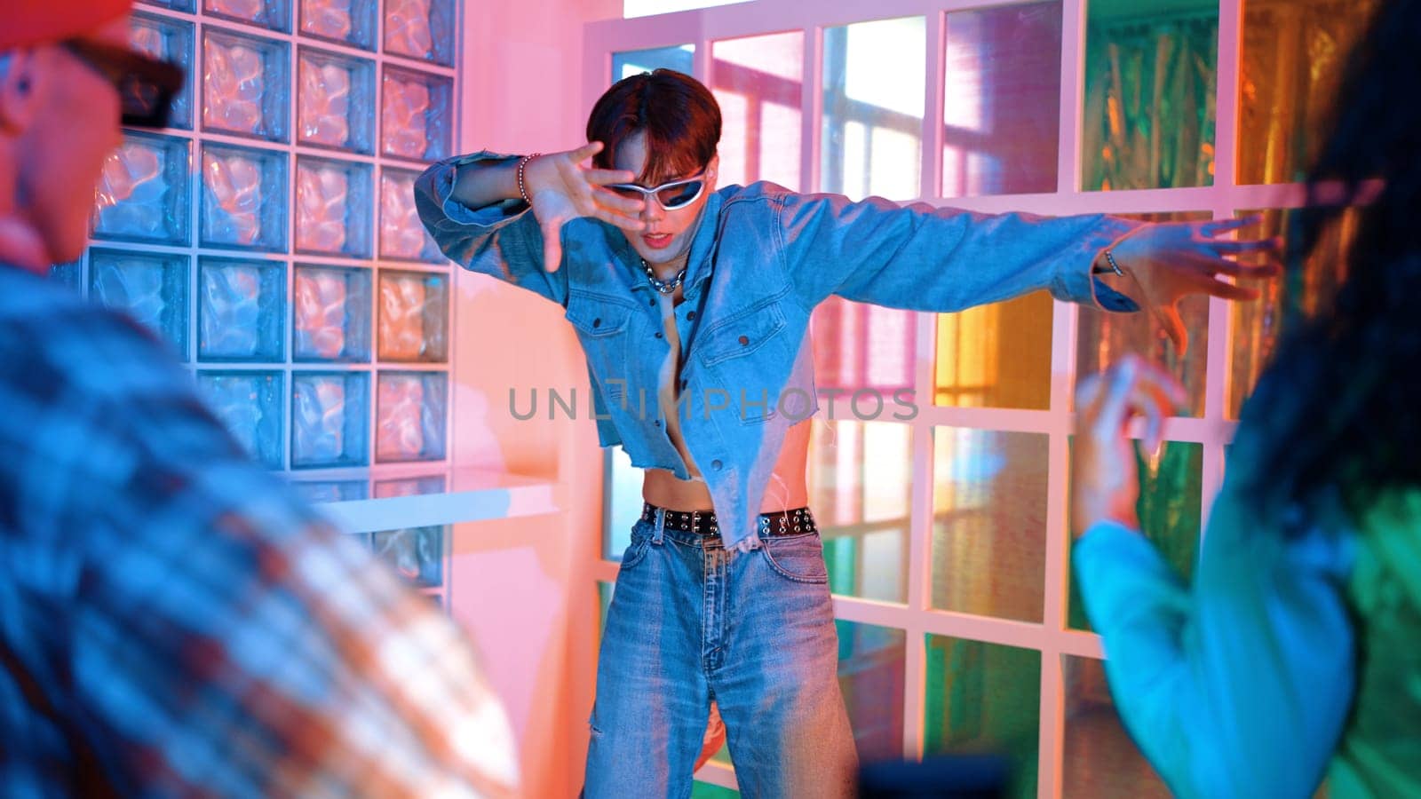 Professional happy hipster moving arm while dancing at center surrounded by diverse friend cheering him. Attractive asian break performing energetic footstep with neon light at nightclub. Regalement.
