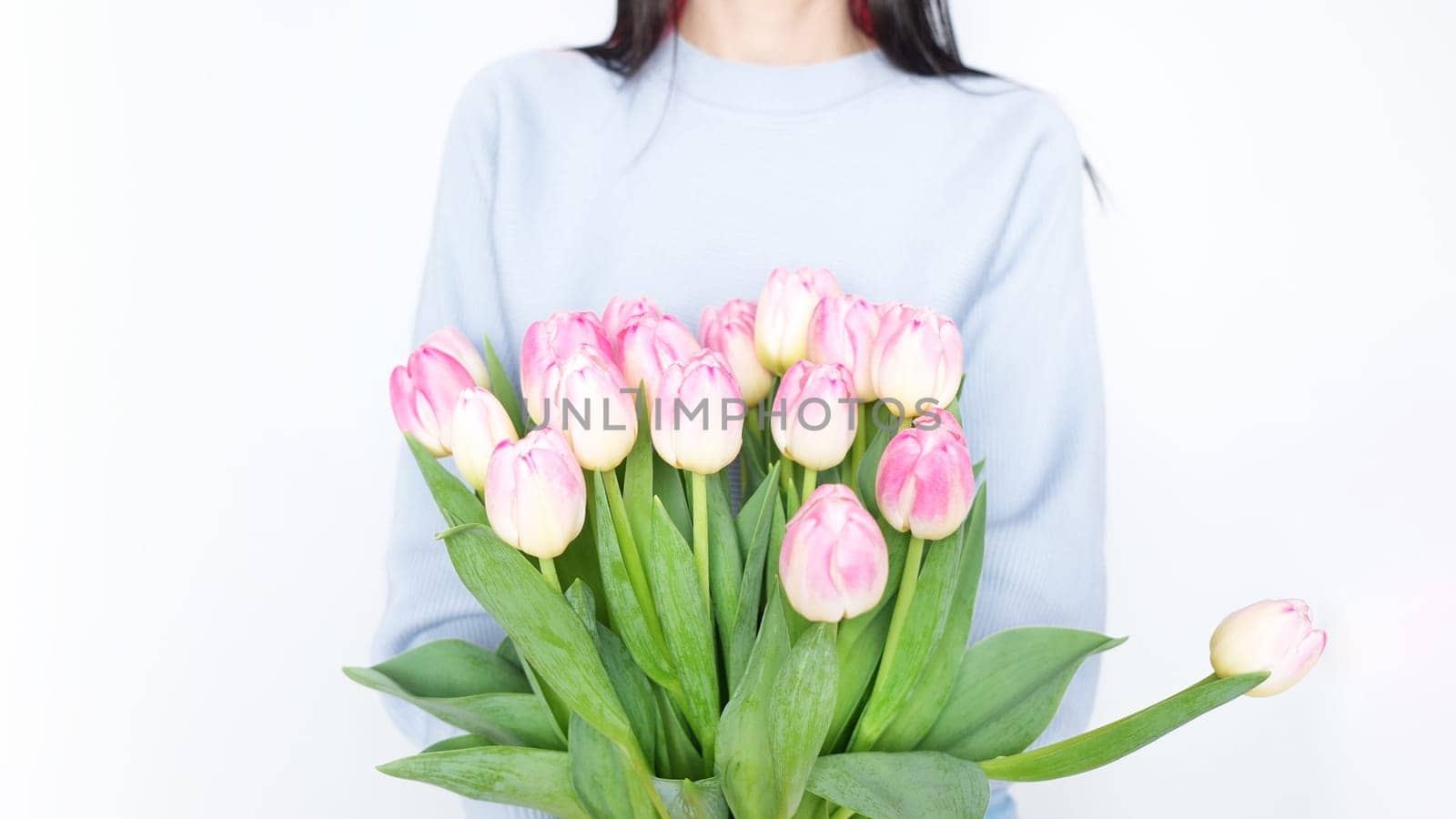 Woman holding a beautiful bouquet of vibrant pink tulips with green foliage against a white background. The pink tulips are striking and complement the womans attire perfectly.