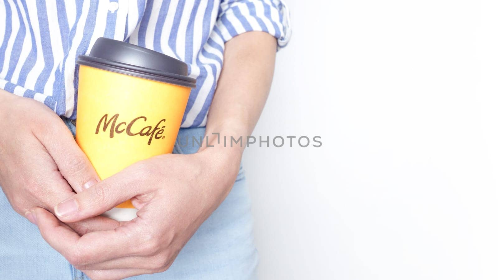 Woman holding a yellow McCafe coffee cup wearing blue jeans and blue striped shirt. Ottawa ON Canada 06-17-2024.