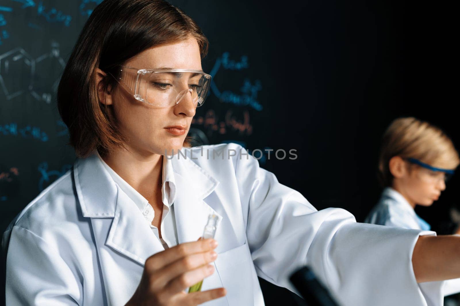 Teacher support schoolboy learning science of chemistry do experiment in laboratory wear lab coat and safety glasses in STEM class. Teacher manage test tube on the table with confidence. Erudition.