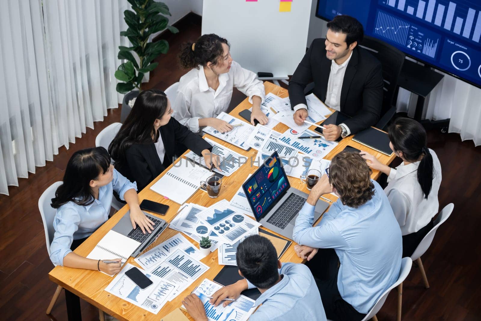 Wide top view of diverse group of business analyst team analyzing financial data report paper on meeting table. Chart and graph dashboard by business intelligence analysis. Meticulous