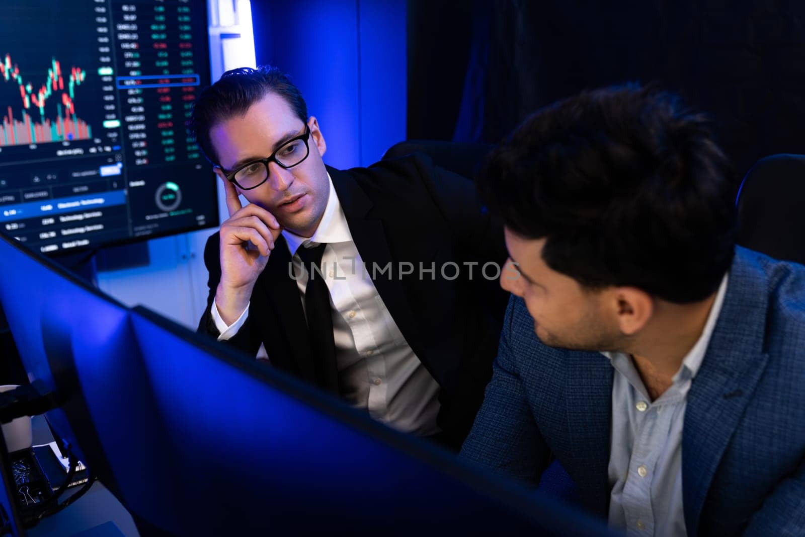 Two stock exchange traders discussing digital currency or market online focusing on dynamic data monitor. Concept of analyzing market stock cooperate at neon blue-light decorative workplace. Sellable.