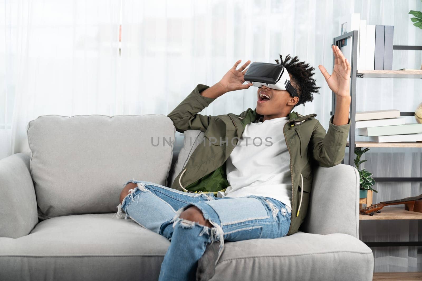 Surprised African American looking VR enjoy watching by touching the air in fantastic 3D cartoon movie technology virtual reality metaverse journey new world at living room sitting sofa. Contrivance.