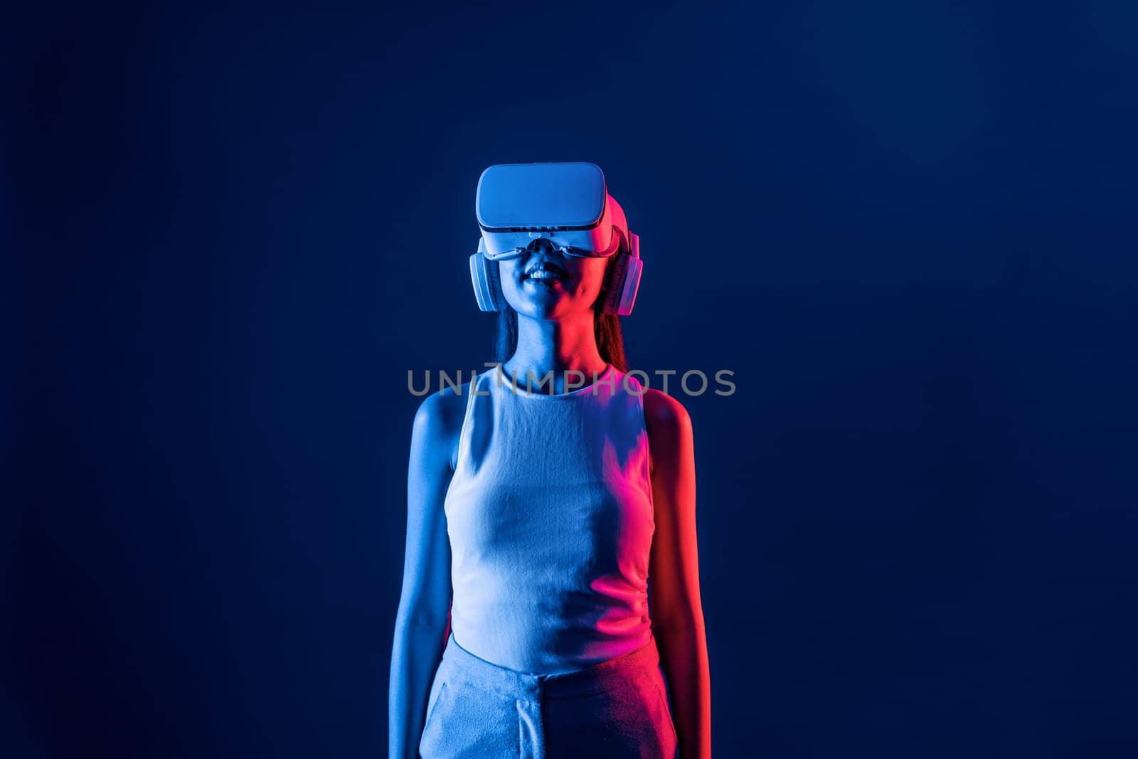 Smart female stand with surrounded by cyberpunk neon light wear VR headset connecting metaverse, futuristic cyberspace community technology. Elegant woman look generated virtual area. Hallucination.