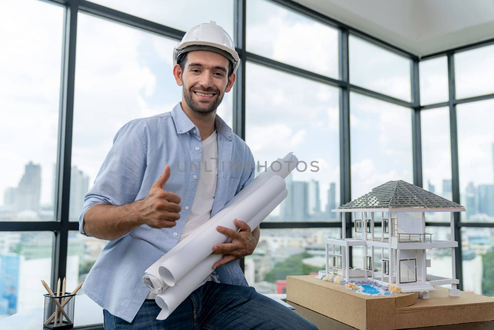 Portrait of professional architect engineer thinking about modern house project while wearing safety helmet and casual outfit. Smart interior designer holding project plans near house model. Tracery.