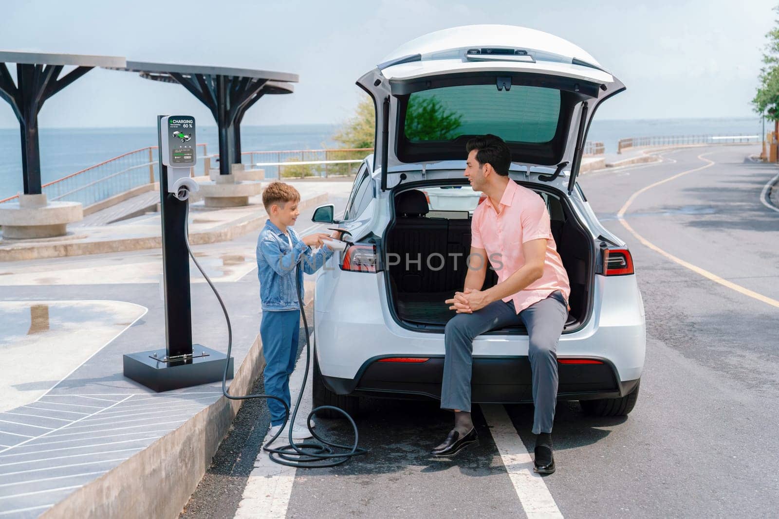 Family road trip vacation traveling by the sea with electric car, father and son recharge EV car with green and clean energy. Natural travel and eco-friendly car for sustainable environment. Perpetual