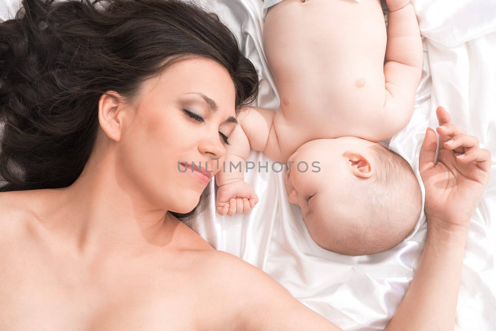 Family portrait. Top view of beautiful young mom and her cute little baby sleeping in bed at home