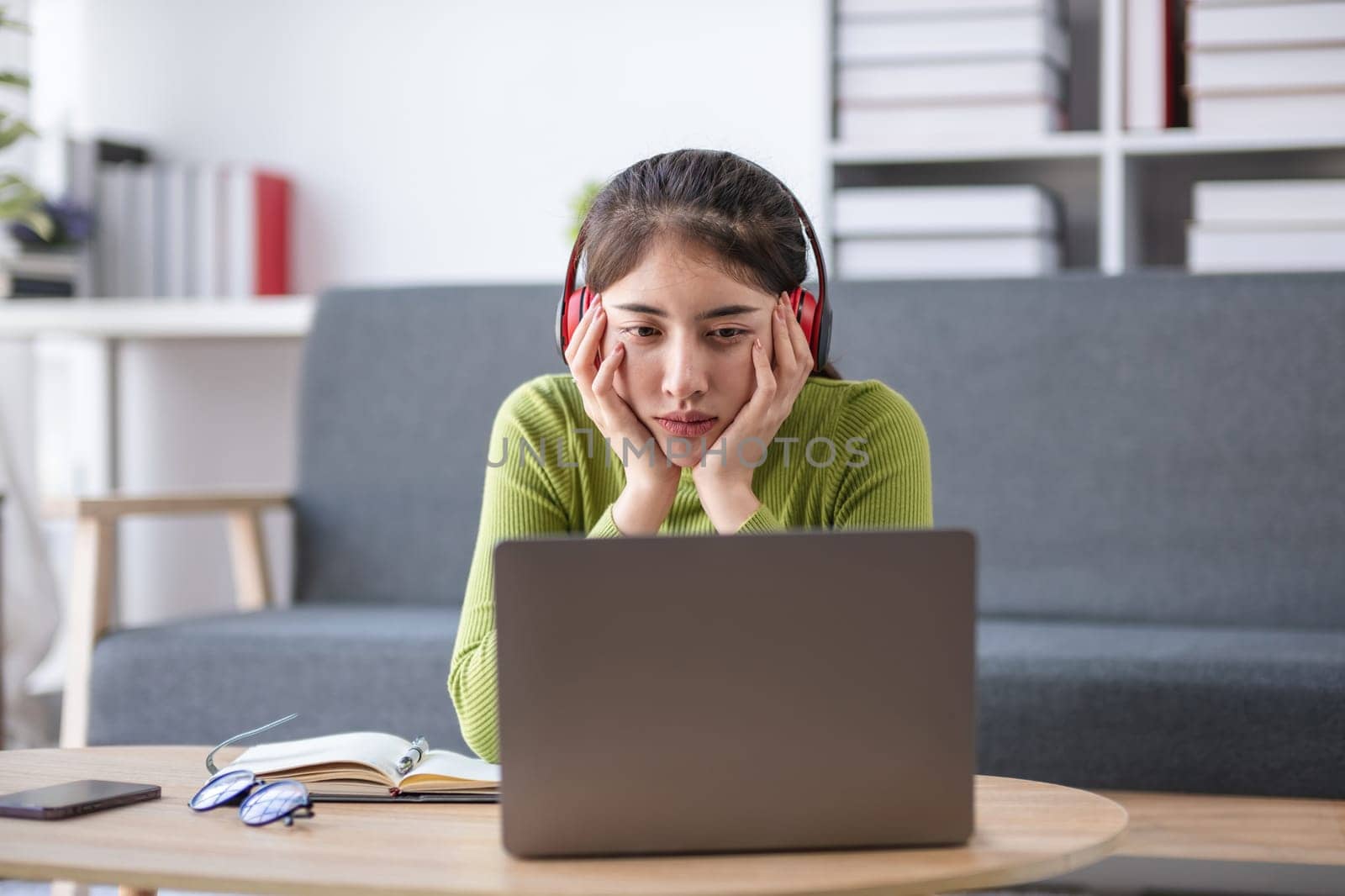 Asian woman feeling stressed while working on laptop with headphones in modern office, concept of stress.