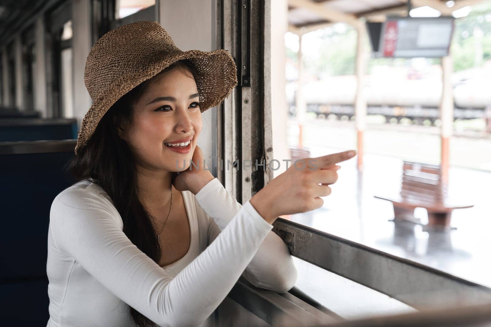 Asian woman pointing out train window with excitement, concept of exploration.