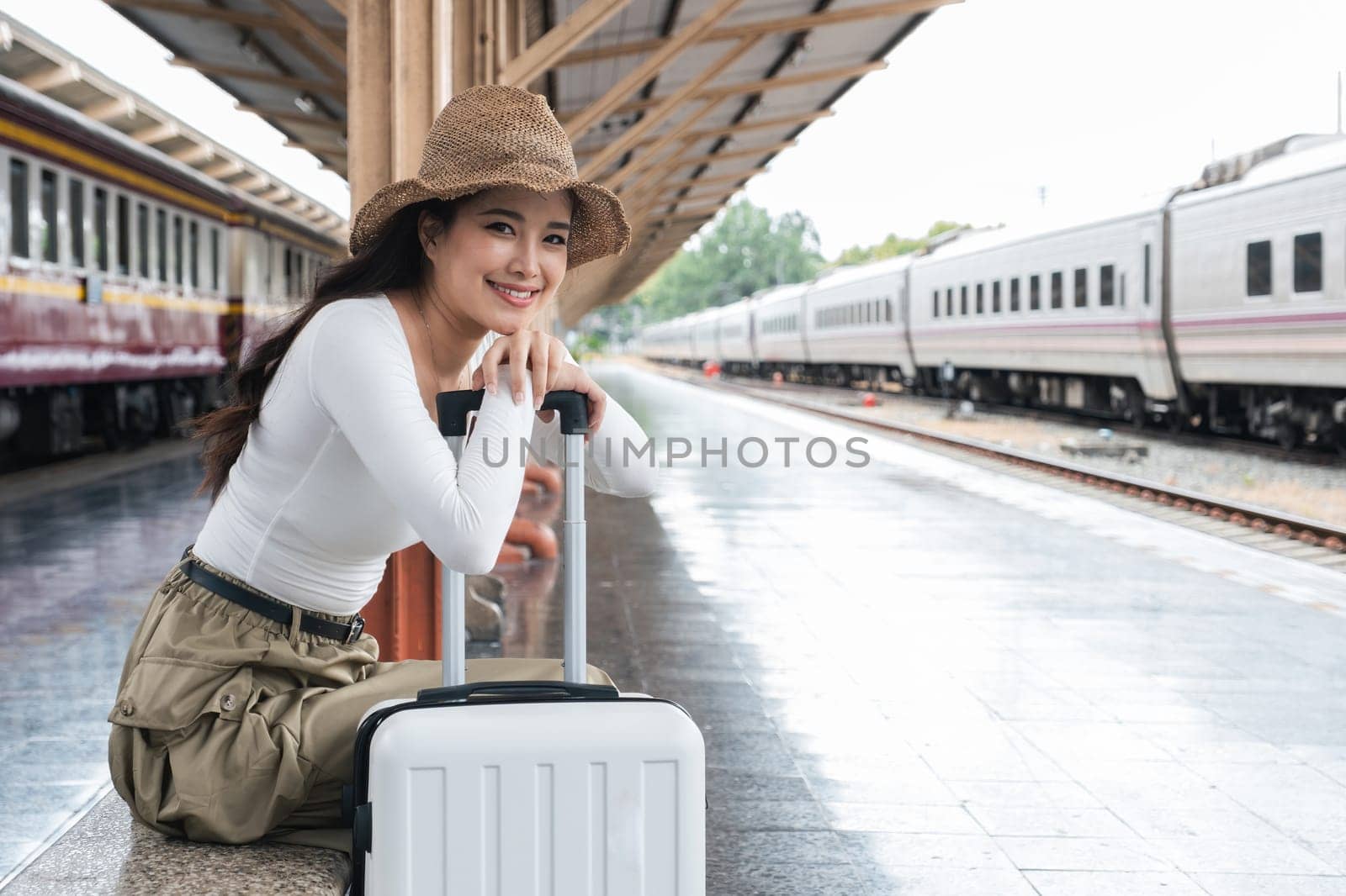 Asian woman waiting at train station with suitcase, concept of travel anticipation.