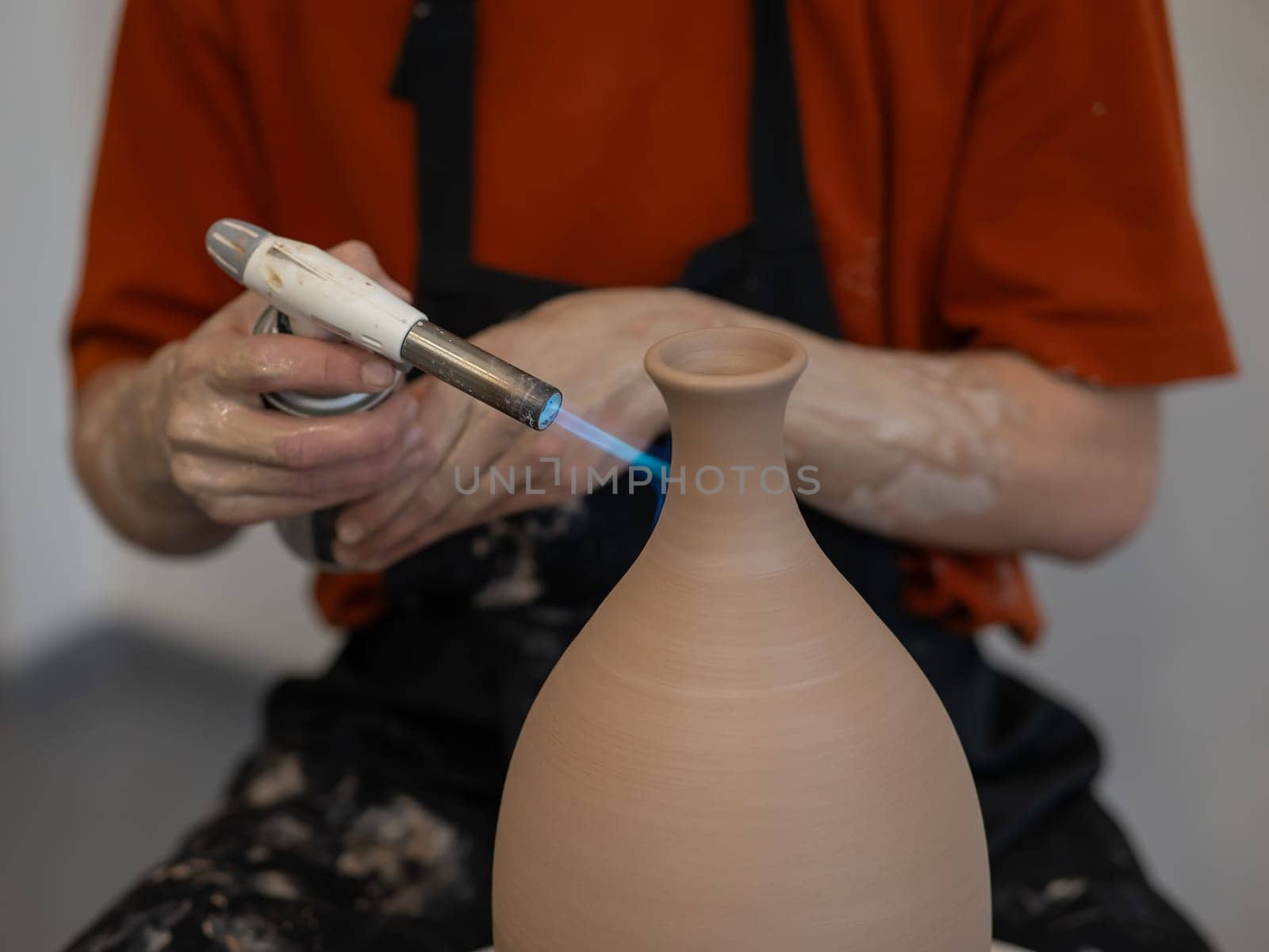 Close-up of a potter's hands firing a jug with a gas burner on a potter's wheel. by mrwed54