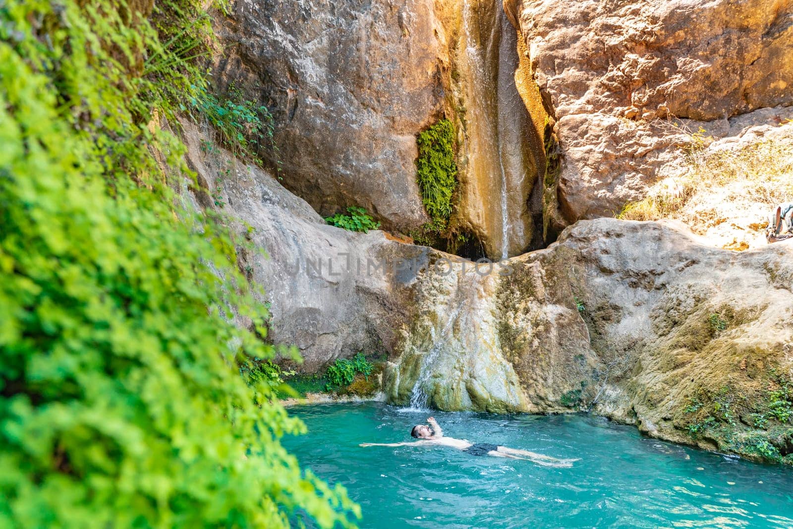 Young happy man floating in turquoise blue crystal clear water in the river with a waterfall summer vacation relaxing body and mind. by PaulCarr